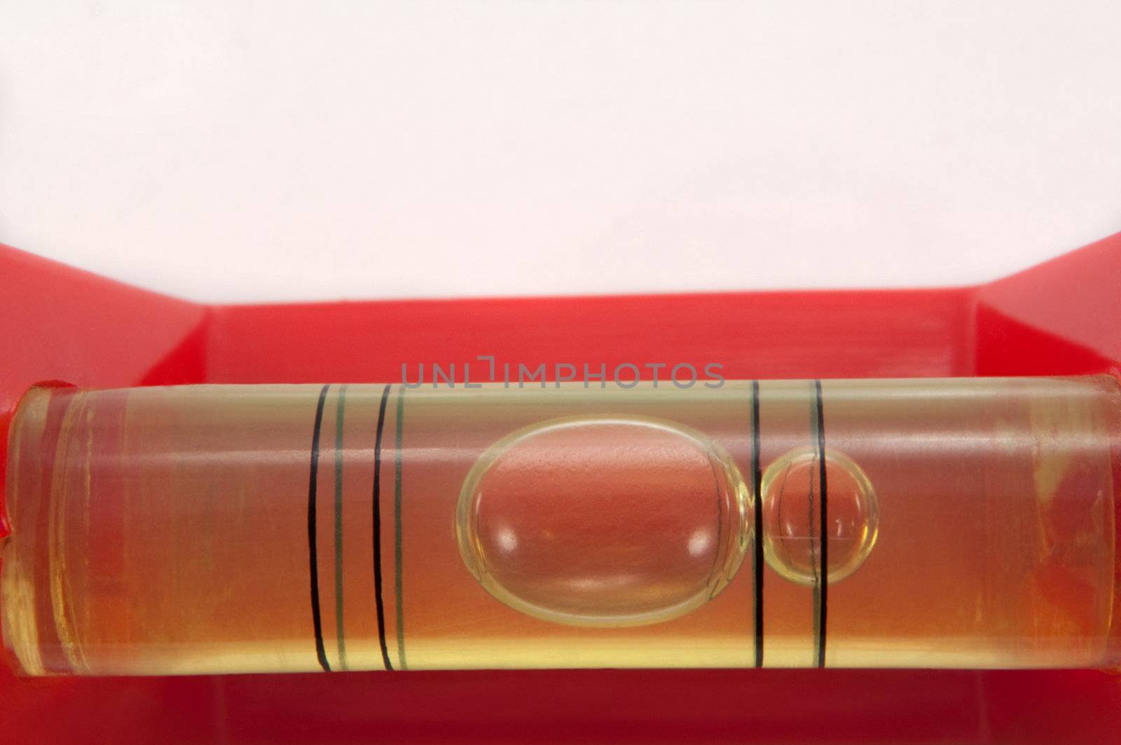 Close up of a red spirit level captured horizontally in the lower portion of the image with white above.