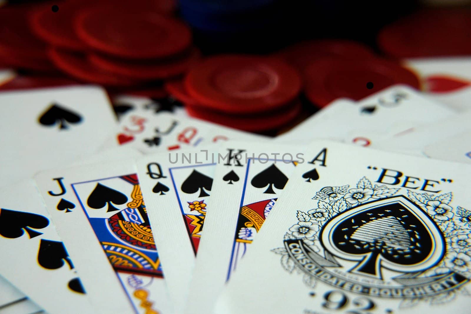 A royal flush poker hand shown face up over a pile of assorted cards and poker chips