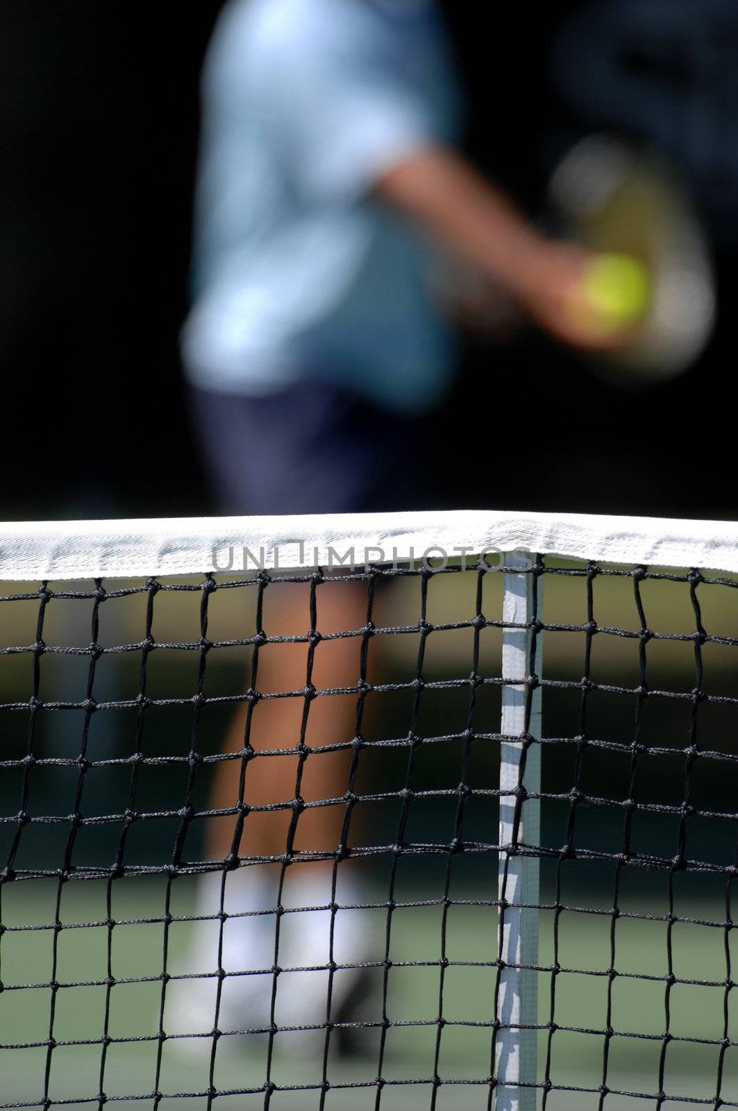 a net with a tennis player preparing to serve in the background