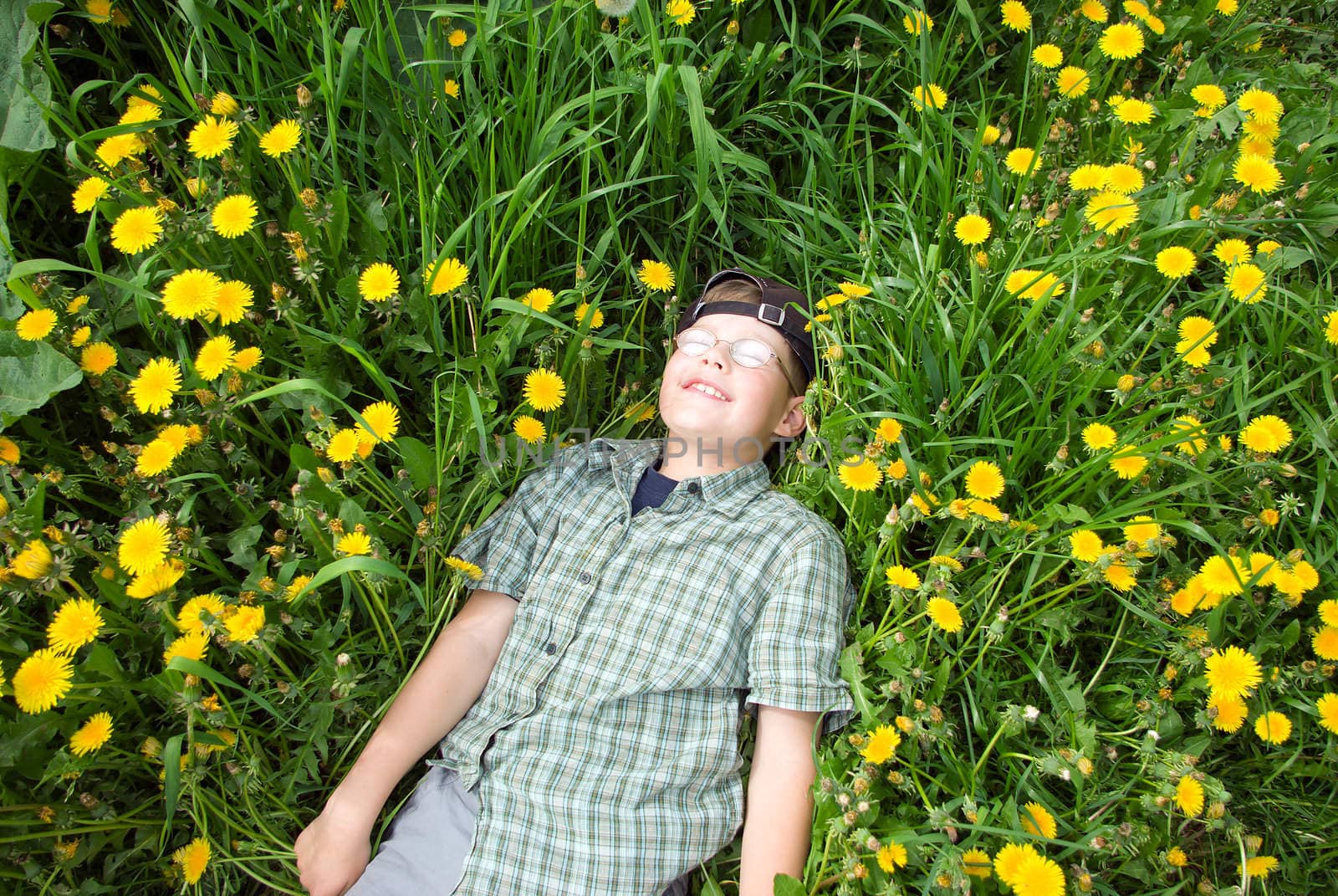 teen boy laying on a beautiful summer dandelion meadow