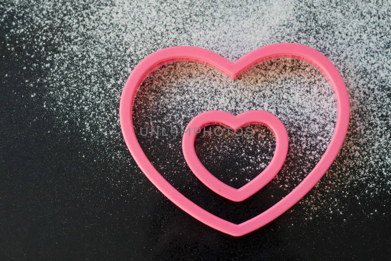 Two heart shaped cookie cutters on a granite worktop, with a dusting of icing sugar