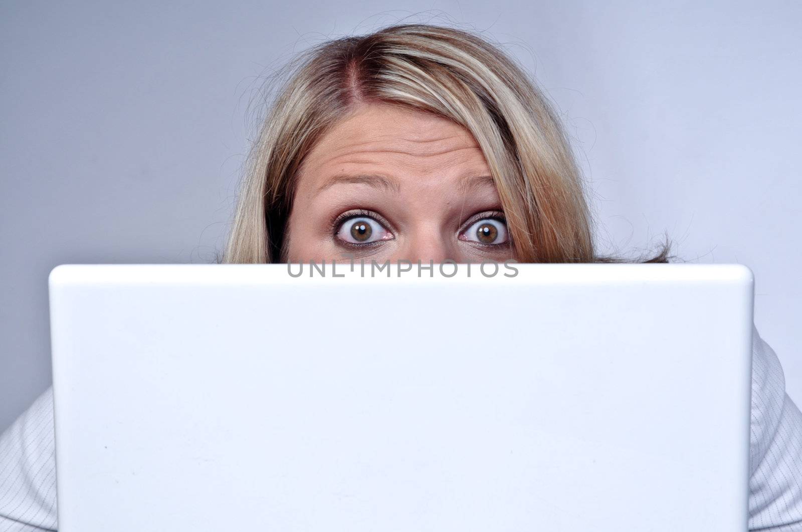 Blond Woman Looking With Eyes Wide Open Behind Laptop