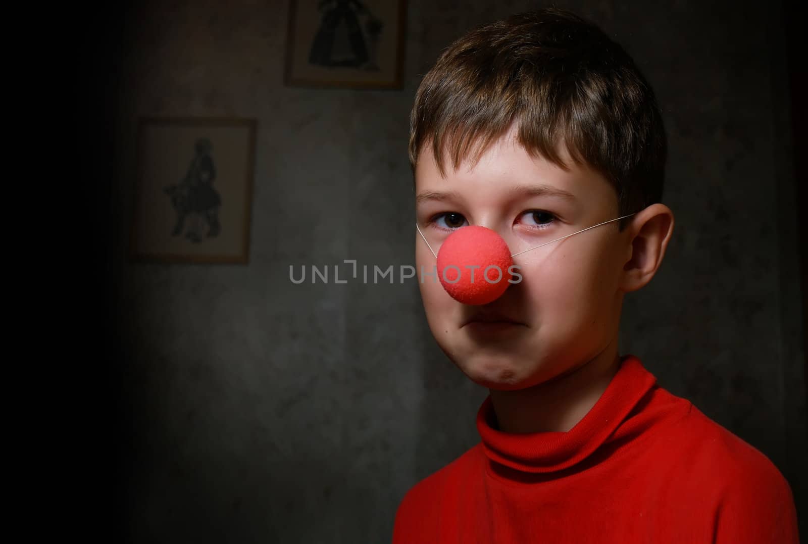 The upset boy with clown's nose in dark room