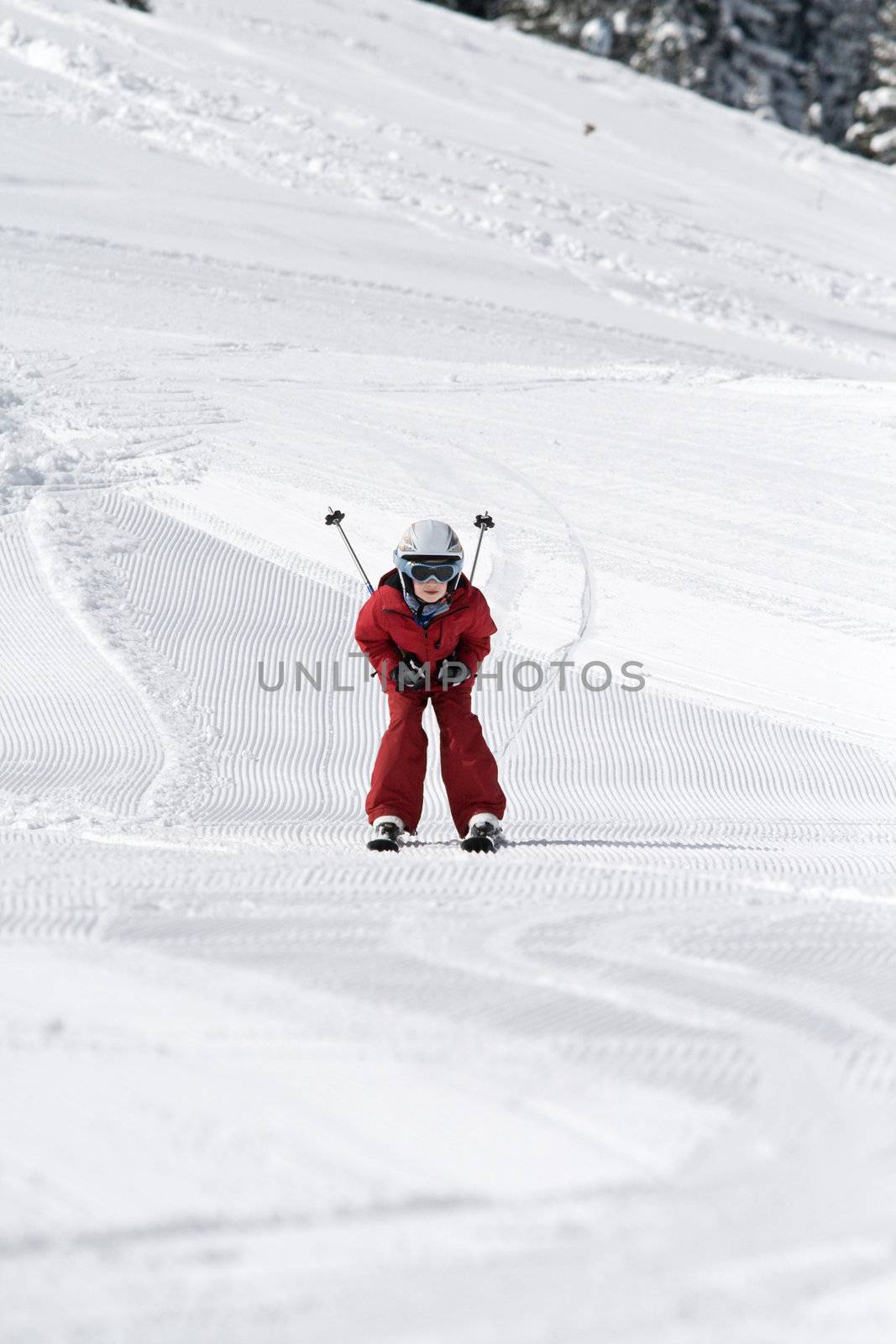 Young boy skiing down a slope, ski poles tucked under his arms