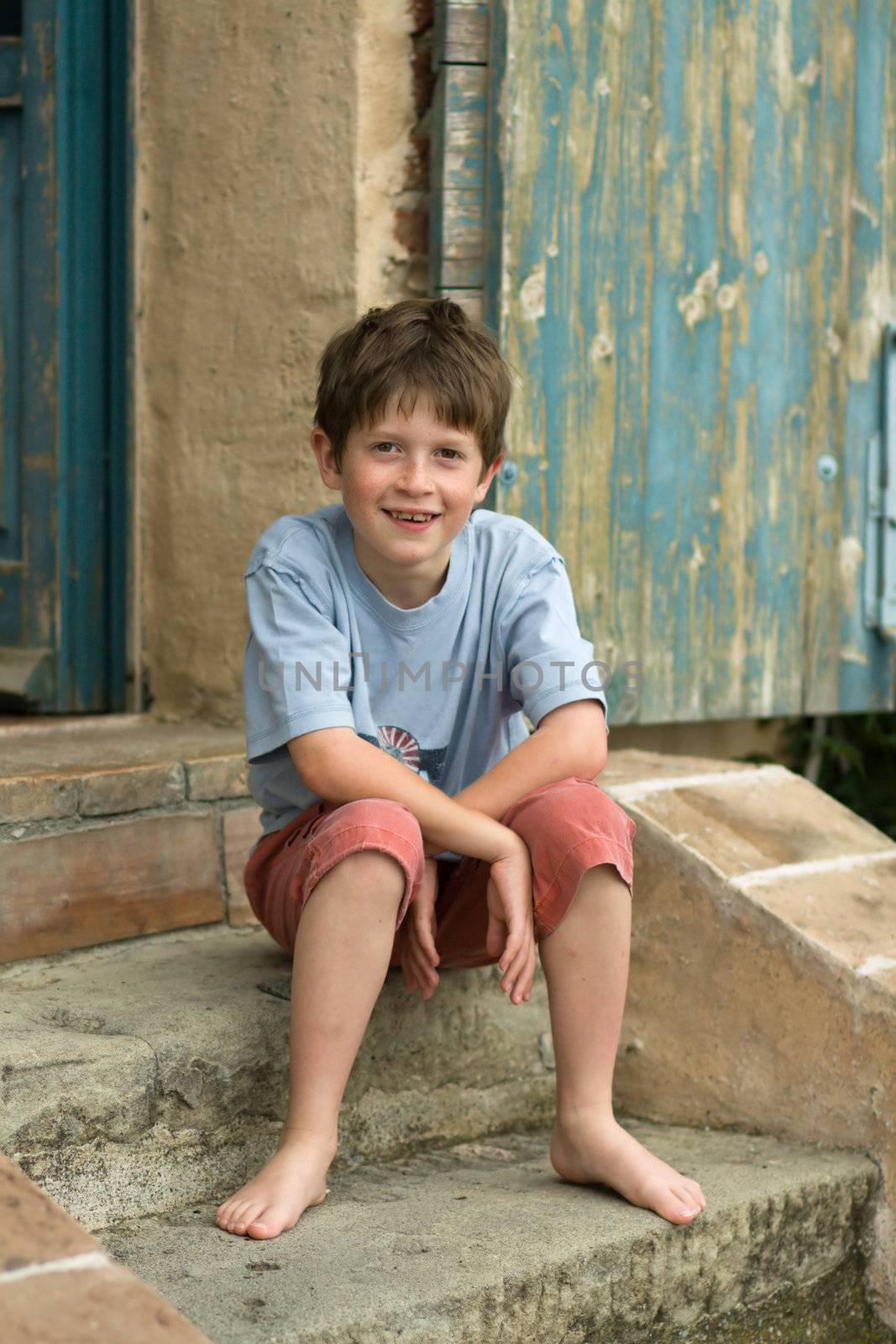 Smiling boy relaxing on the steps of a rustic farmhouse