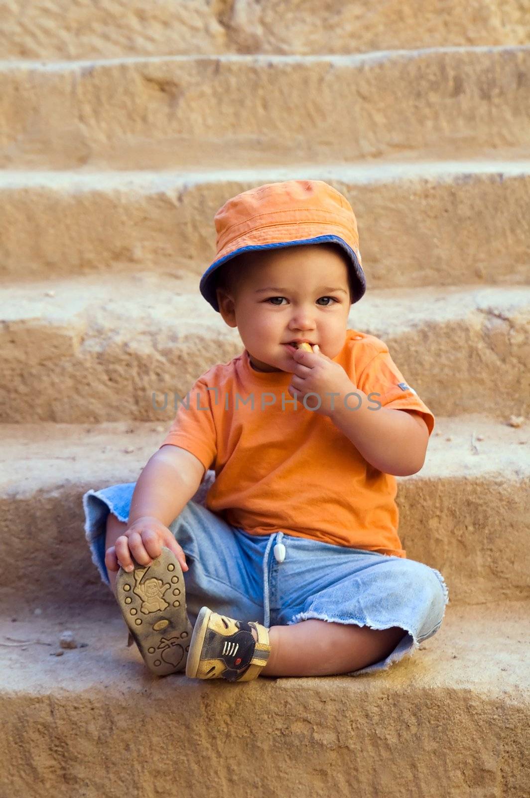 Orange dressed boy sitting on steps and eating