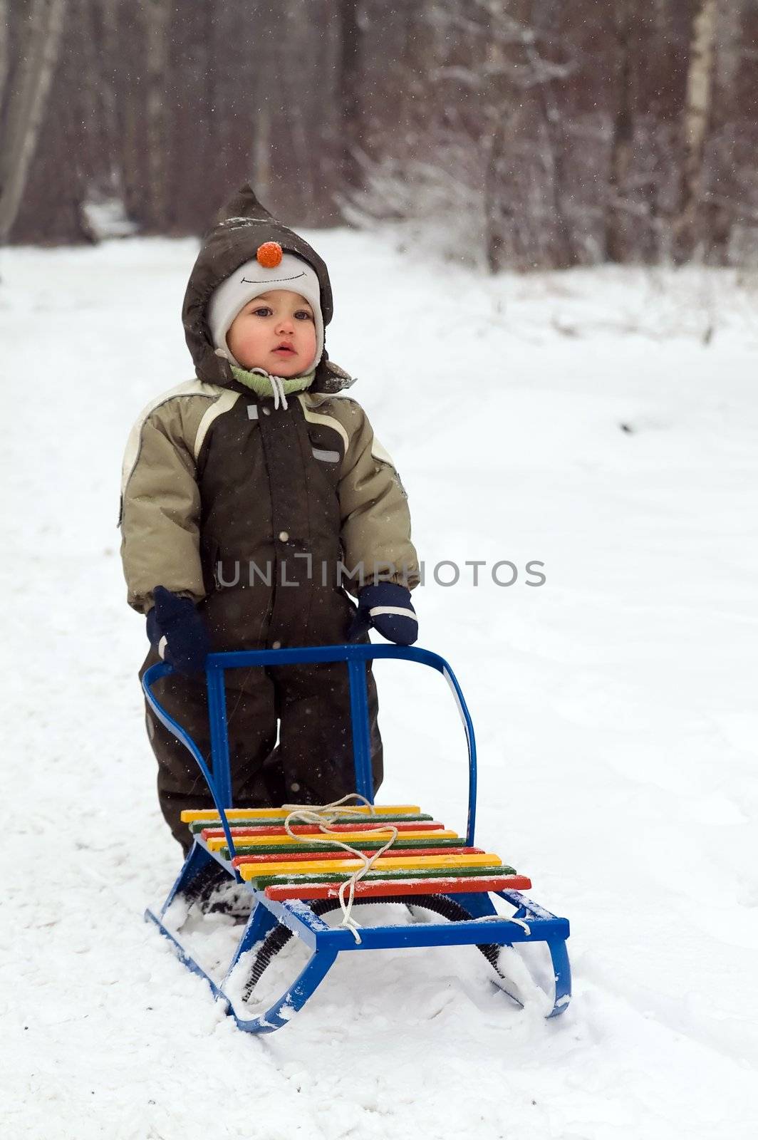 baby in green coat standing near sled in snow-covered park