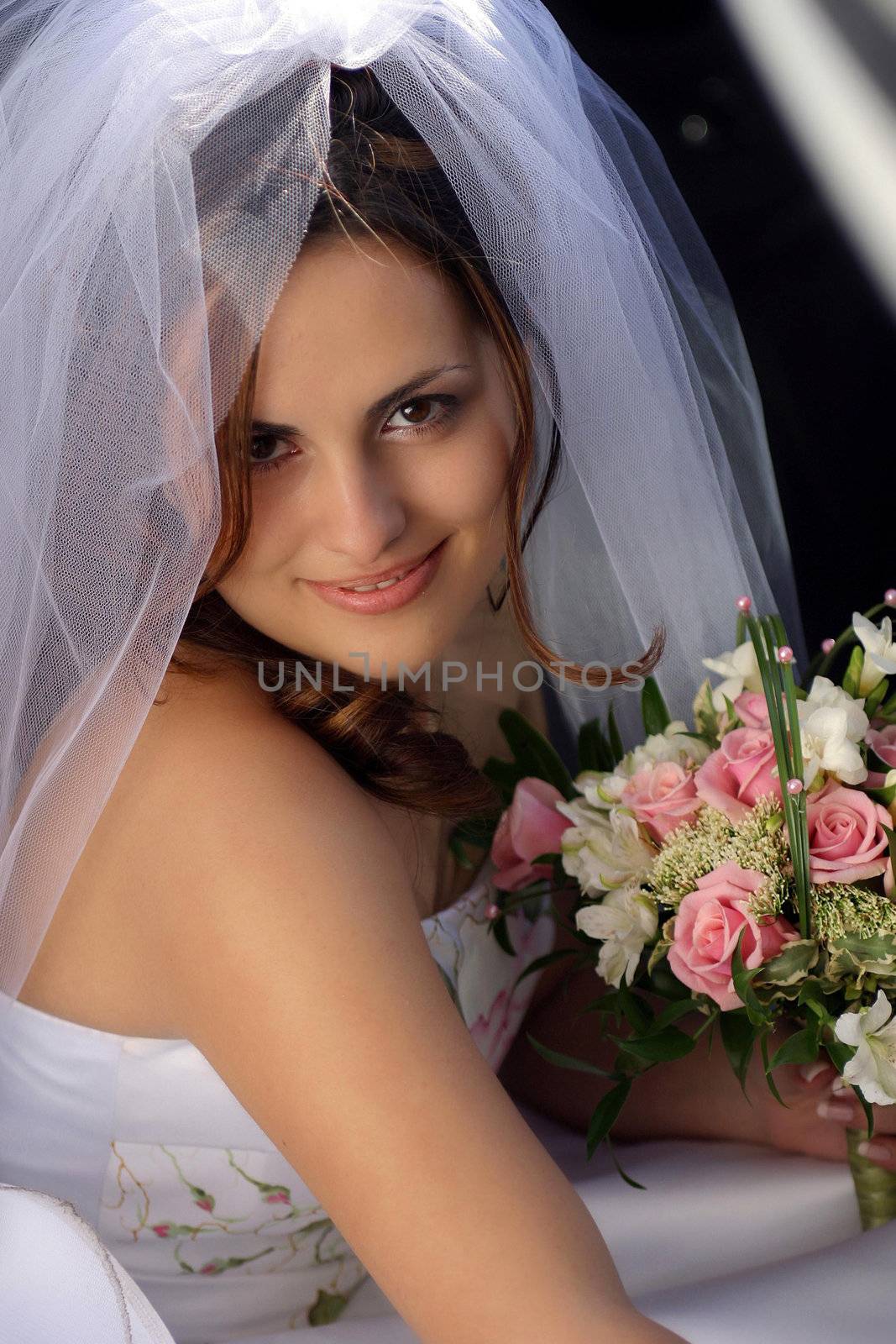 Smiling bride in white on her wedding day, holding bouquet.