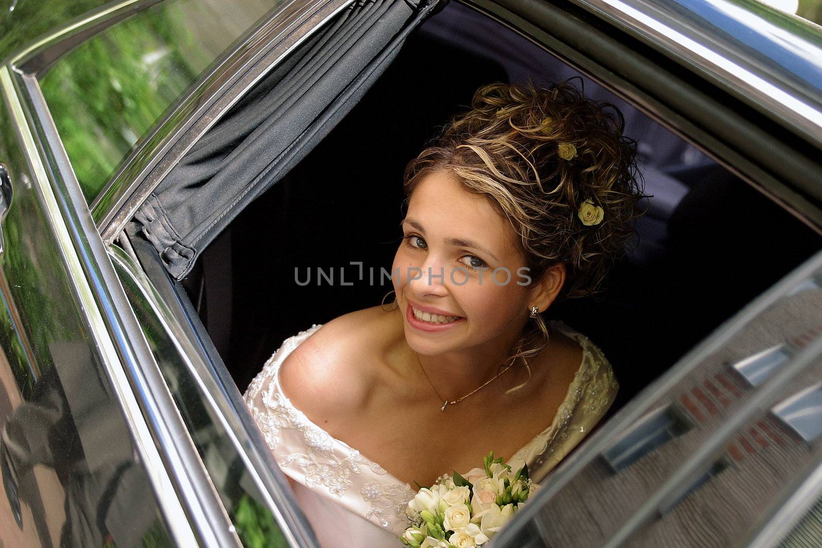 Smiling bride in white on her wedding day, holding bouquet.