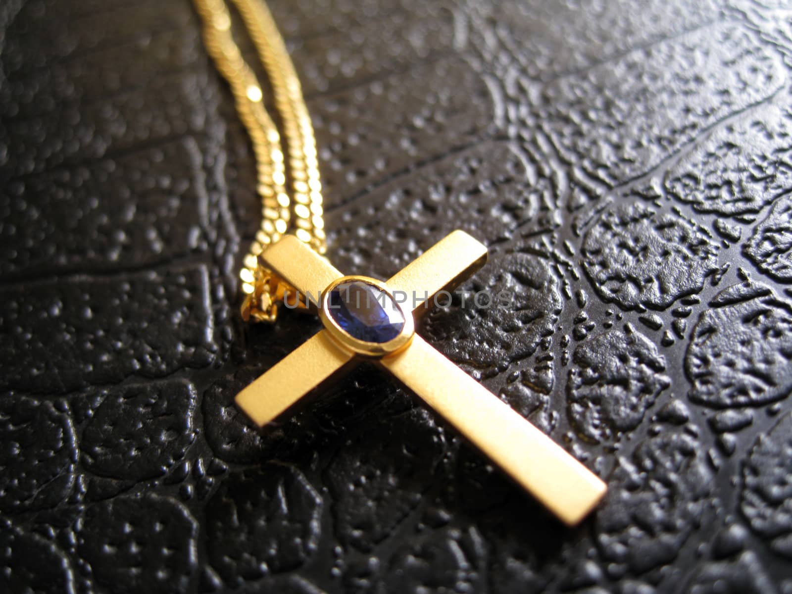 a golden cross necklace with a blue crystal on middle