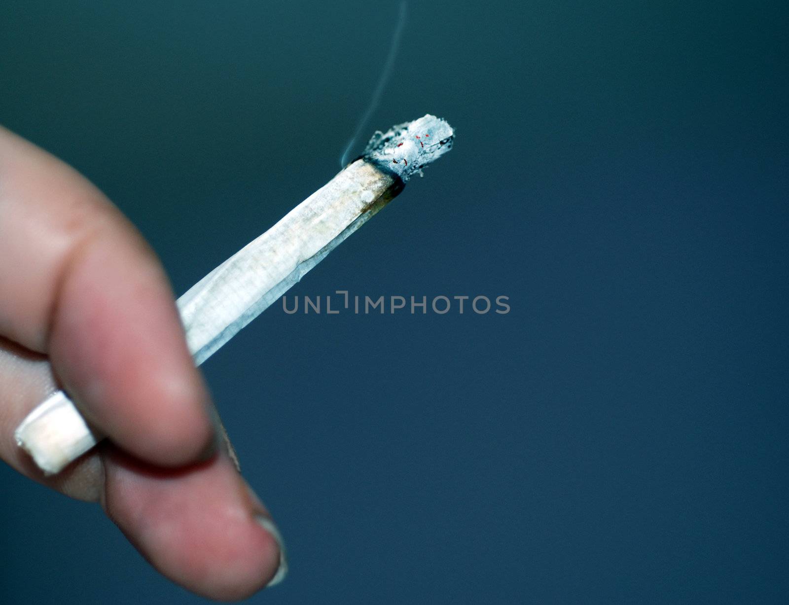 A close up photograph of someone's hand who is smoking a rolled cigarette