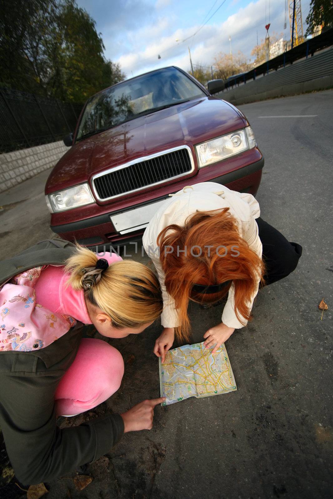 The young girls with a map of streets on a background of the red automobile