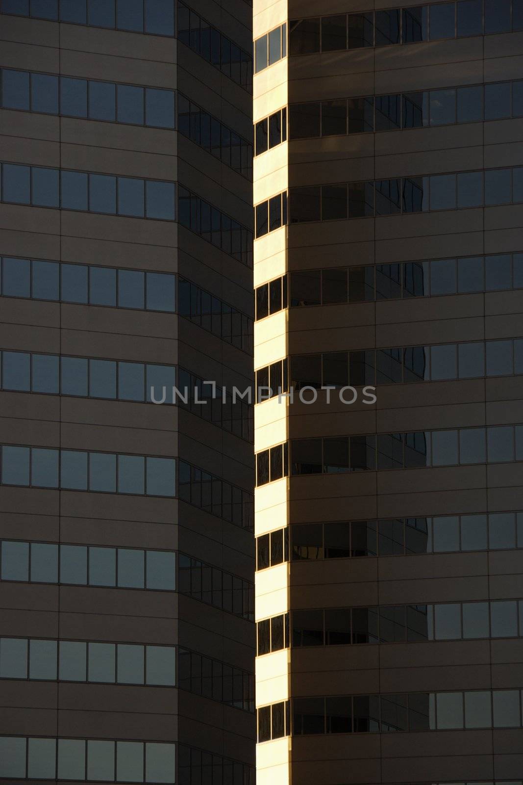 Side exterior of urban skyscraper building with light reflecting off windows.