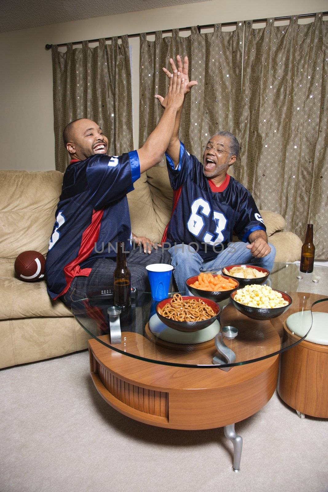 African-American father and son giving high five while watching football game.