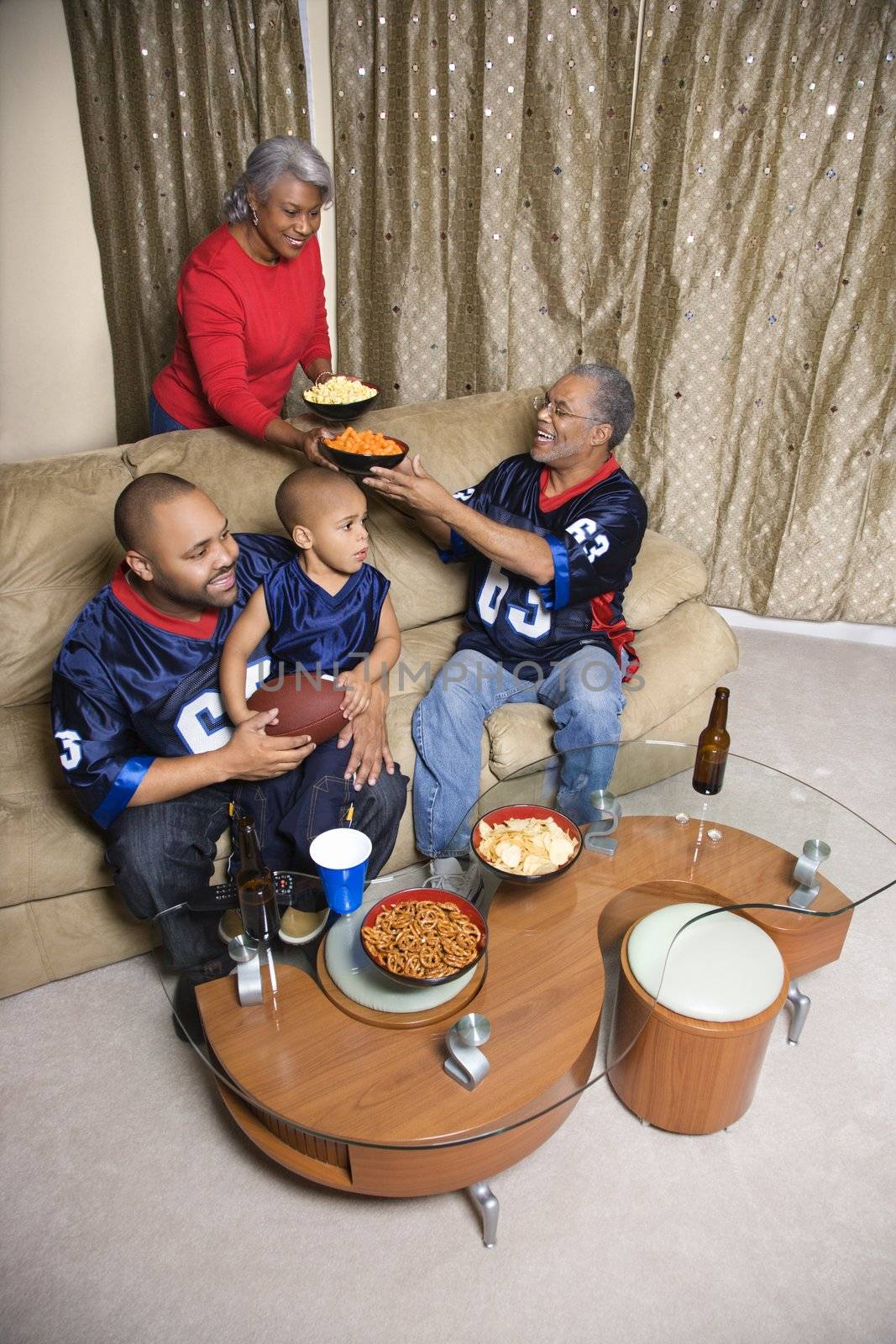 Mother serving snacks to male African-American family members during football game.
