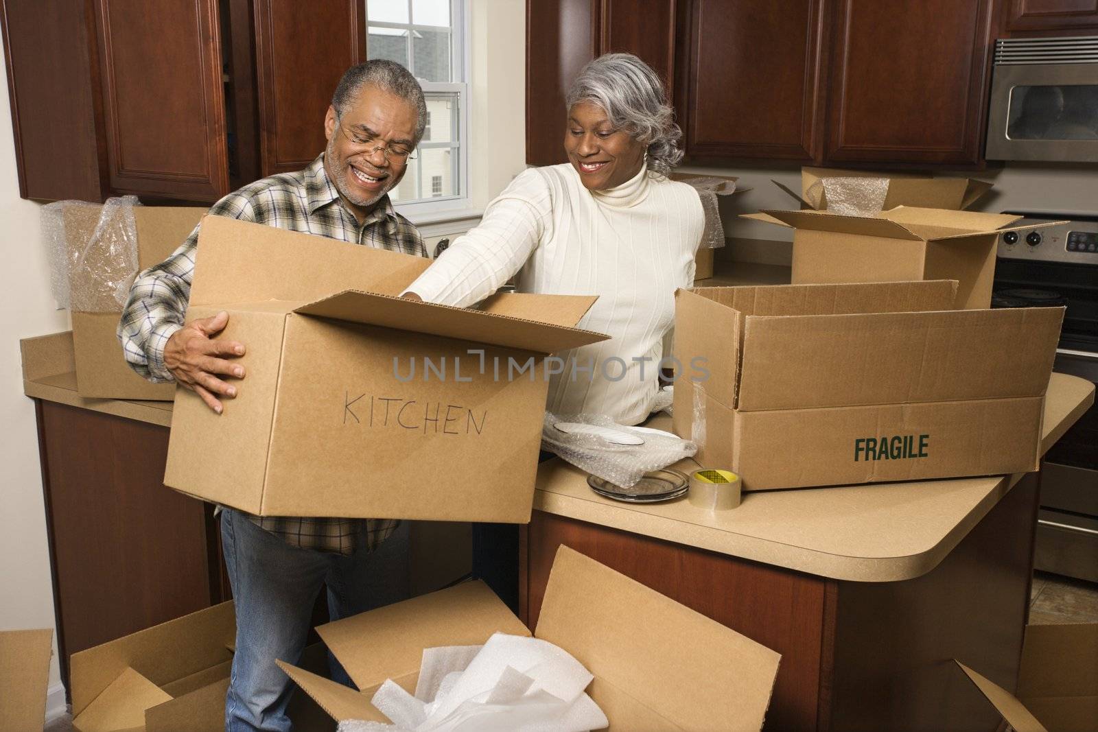 Middle-aged African-American couple packing moving boxes in kitchen.