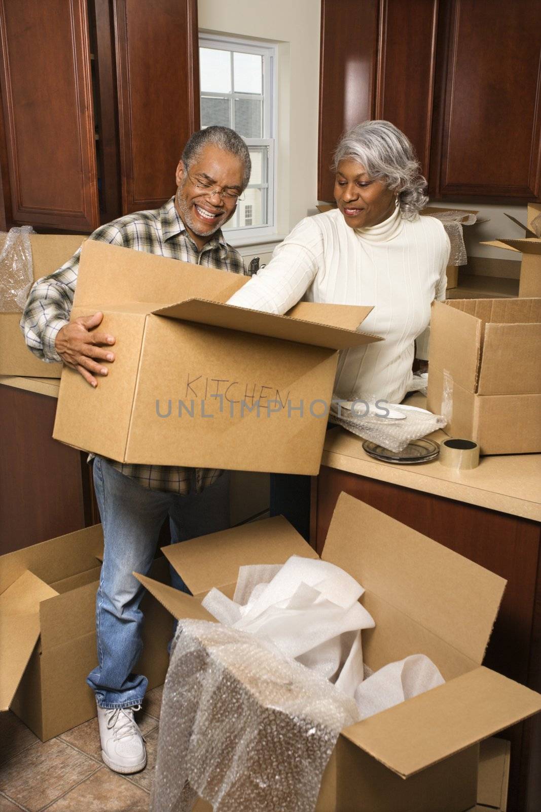 Portrait of middle-aged African-American couple packing moving boxes in kitchen.