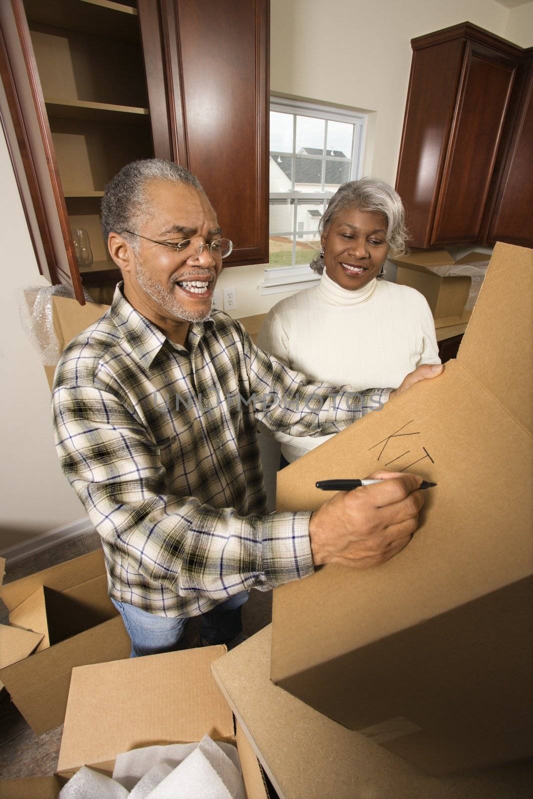 Middle-aged African-American male labeling moving box with wife in background.