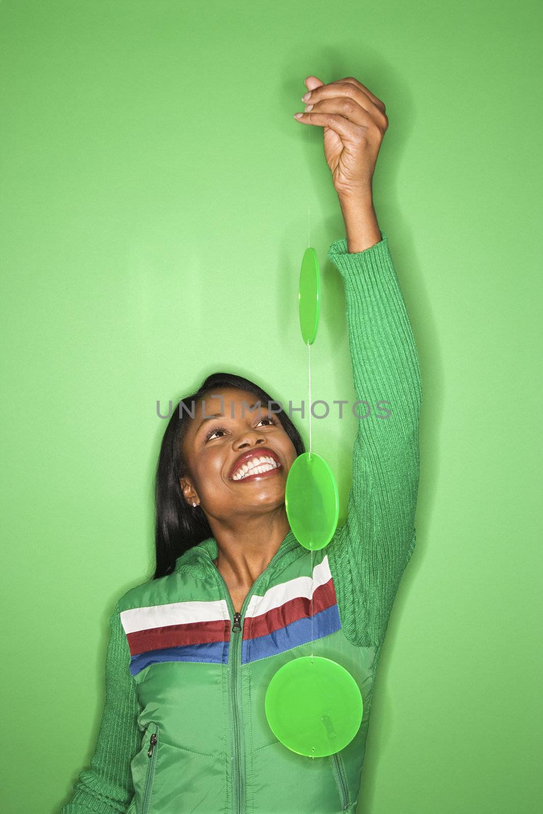 Smiling African-American mid-adult woman in green coat on green background holding green mobile.