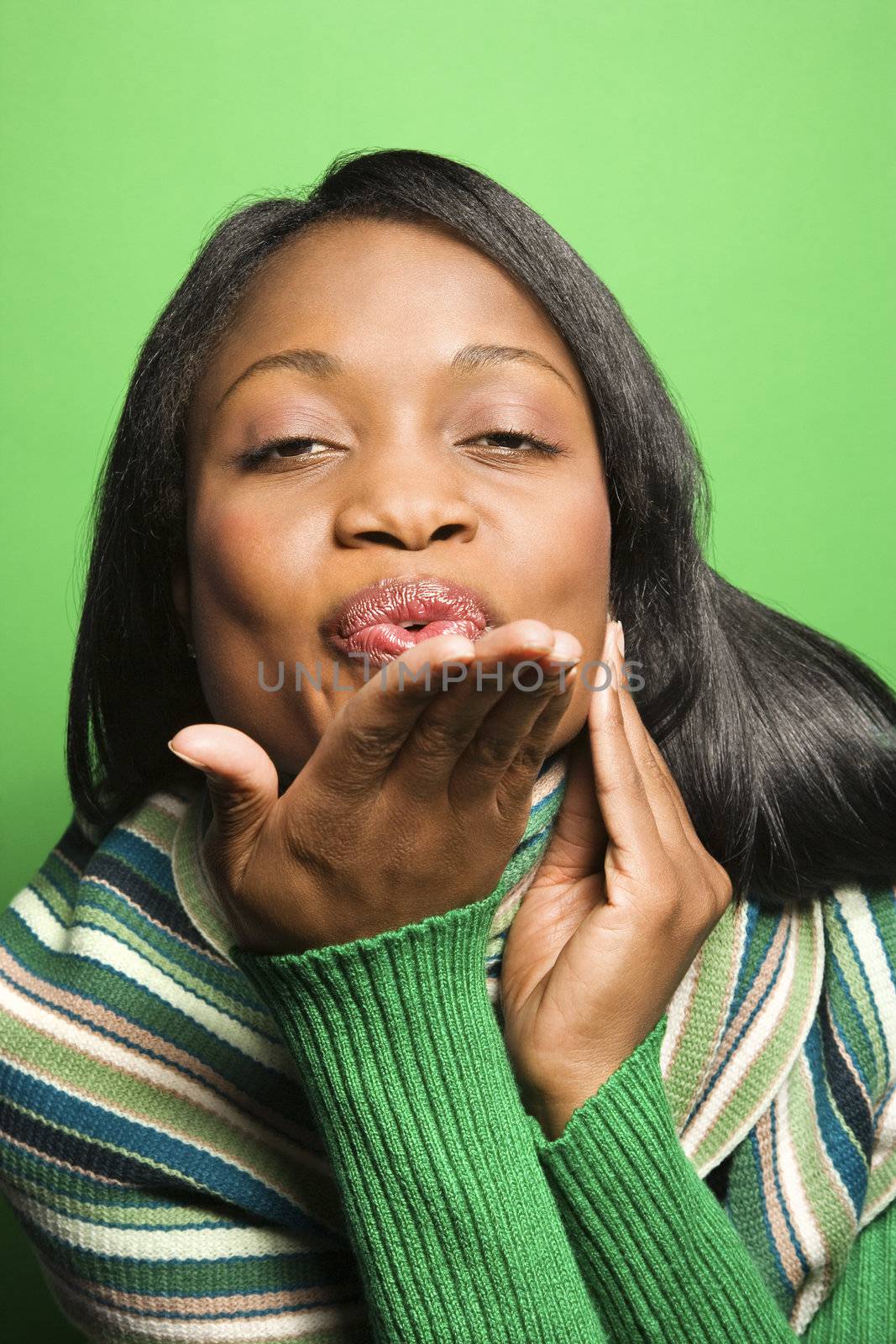 African-American mid-adult woman wearing green scarf on green background blowing kiss at viewer.