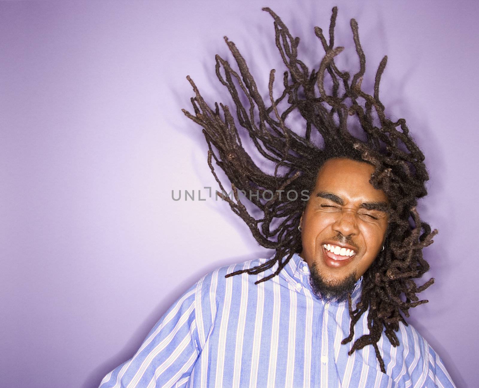 African-American mid-adult man on purple background with his dreadlocks in motion.