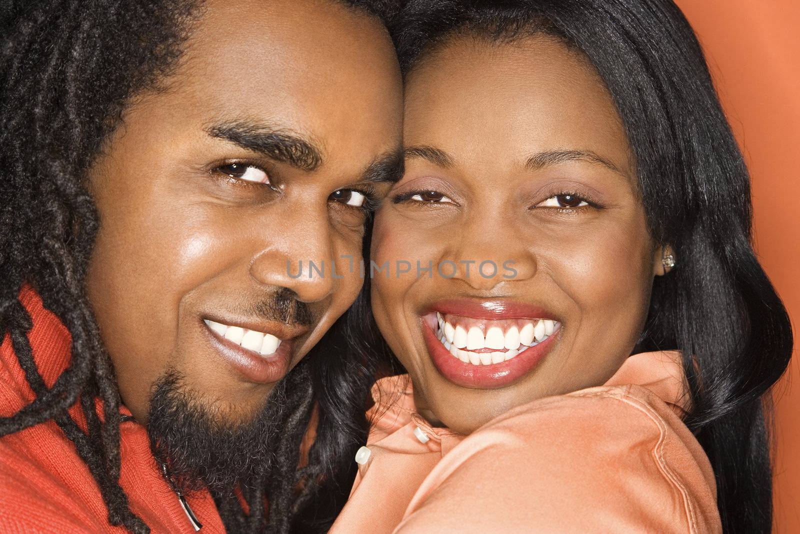 Smiling African-American mid-adult couple wearing orange clothing on orange background.