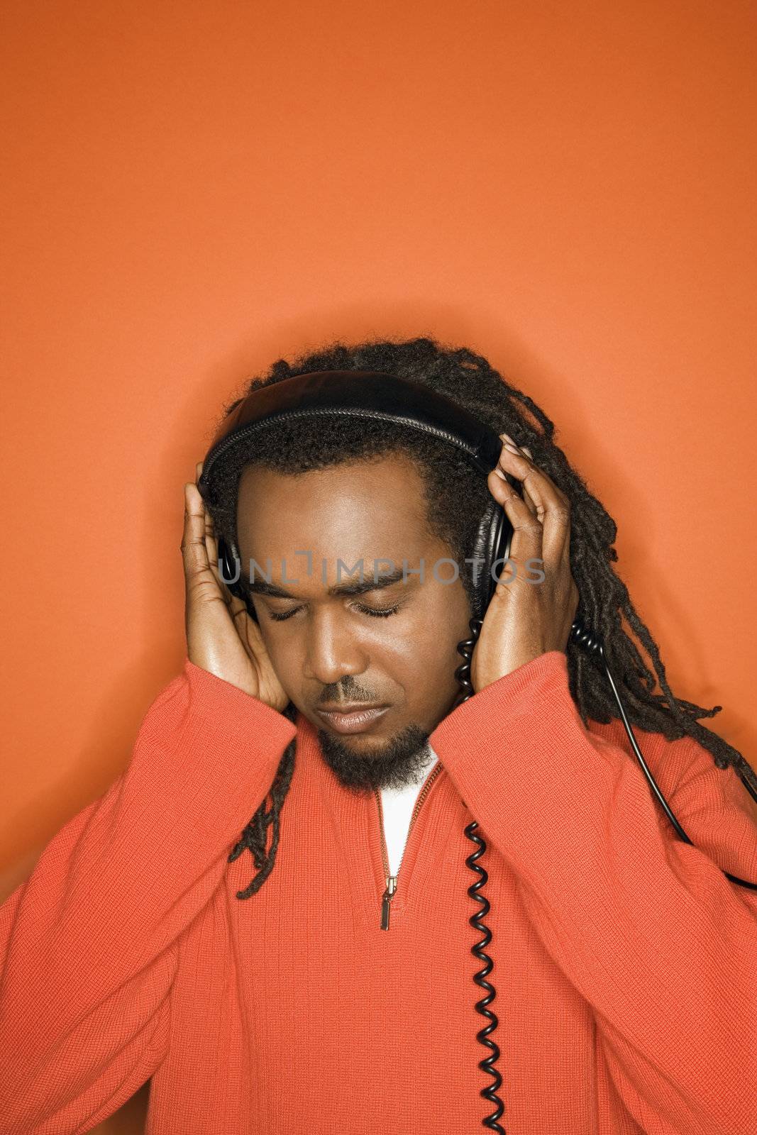 African-American mid-adult listening to headphones wearing orange clothing on orange background.