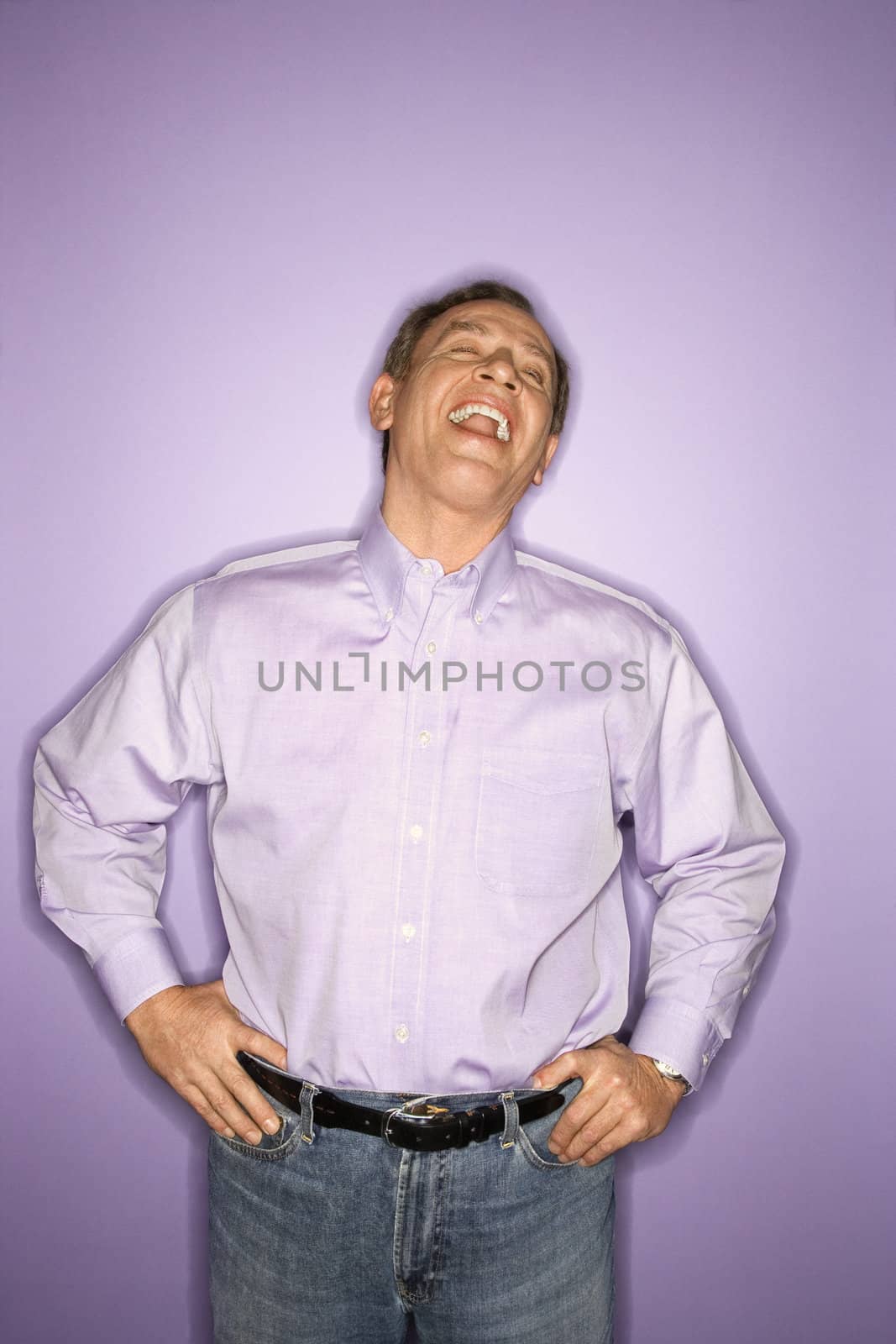 Laughing middle-aged Caucasian man wearing purple clothing on purple background.