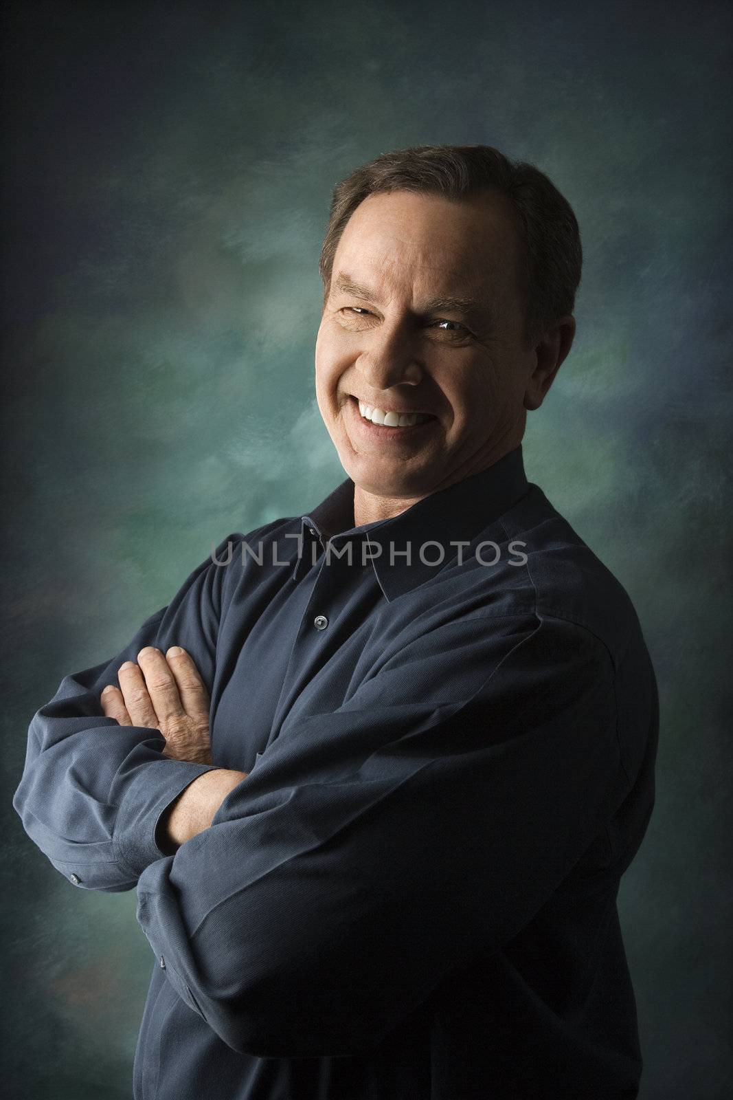 Smiling middle-aged Caucasian man with arms crossed on studio background.