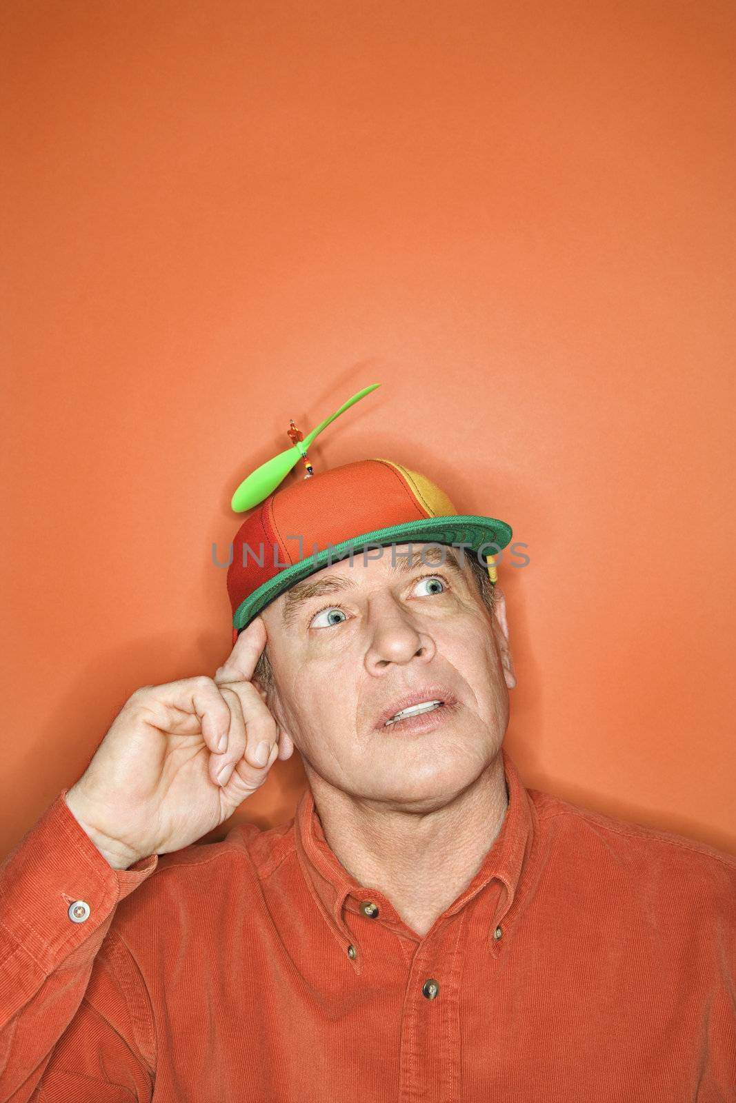 Contemplative niddle-aged Caucasian man wearing propeller cap on orange background.