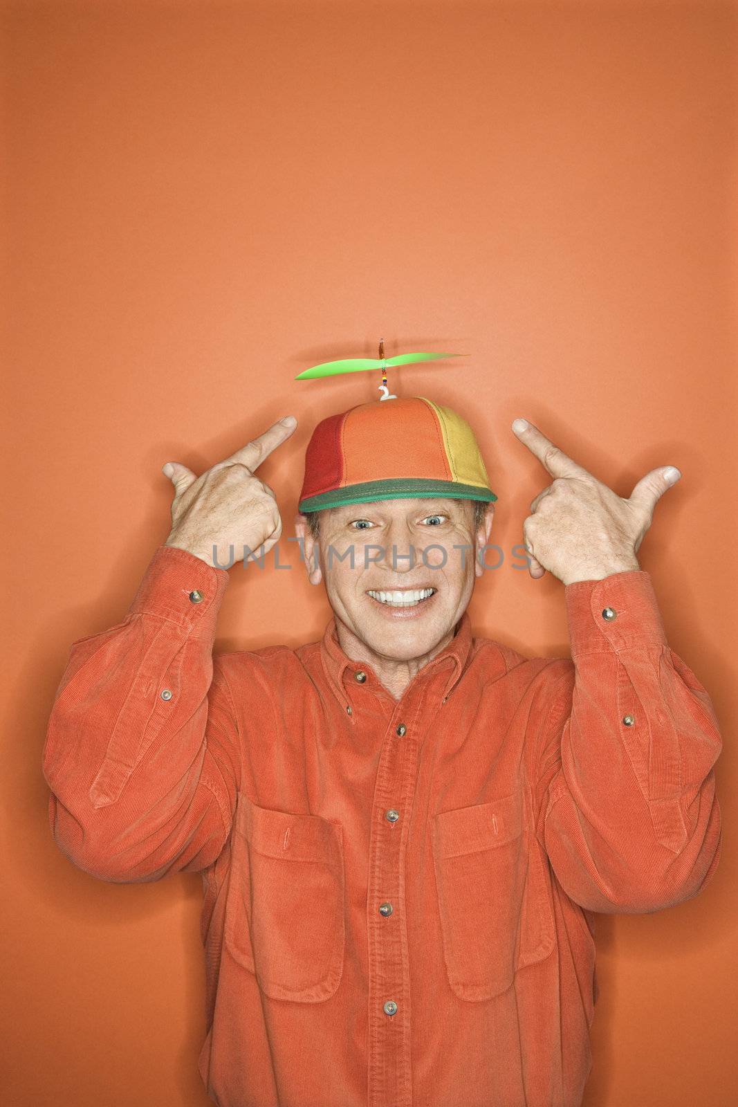 Smiling middle-aged Caucasian man wearing propeller cap on orange background.