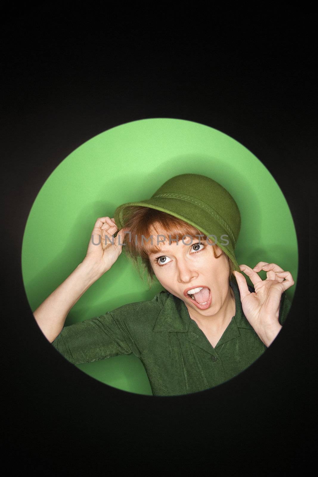 Vignette of Caucasian mid-adult woman tilting hat on green background.
