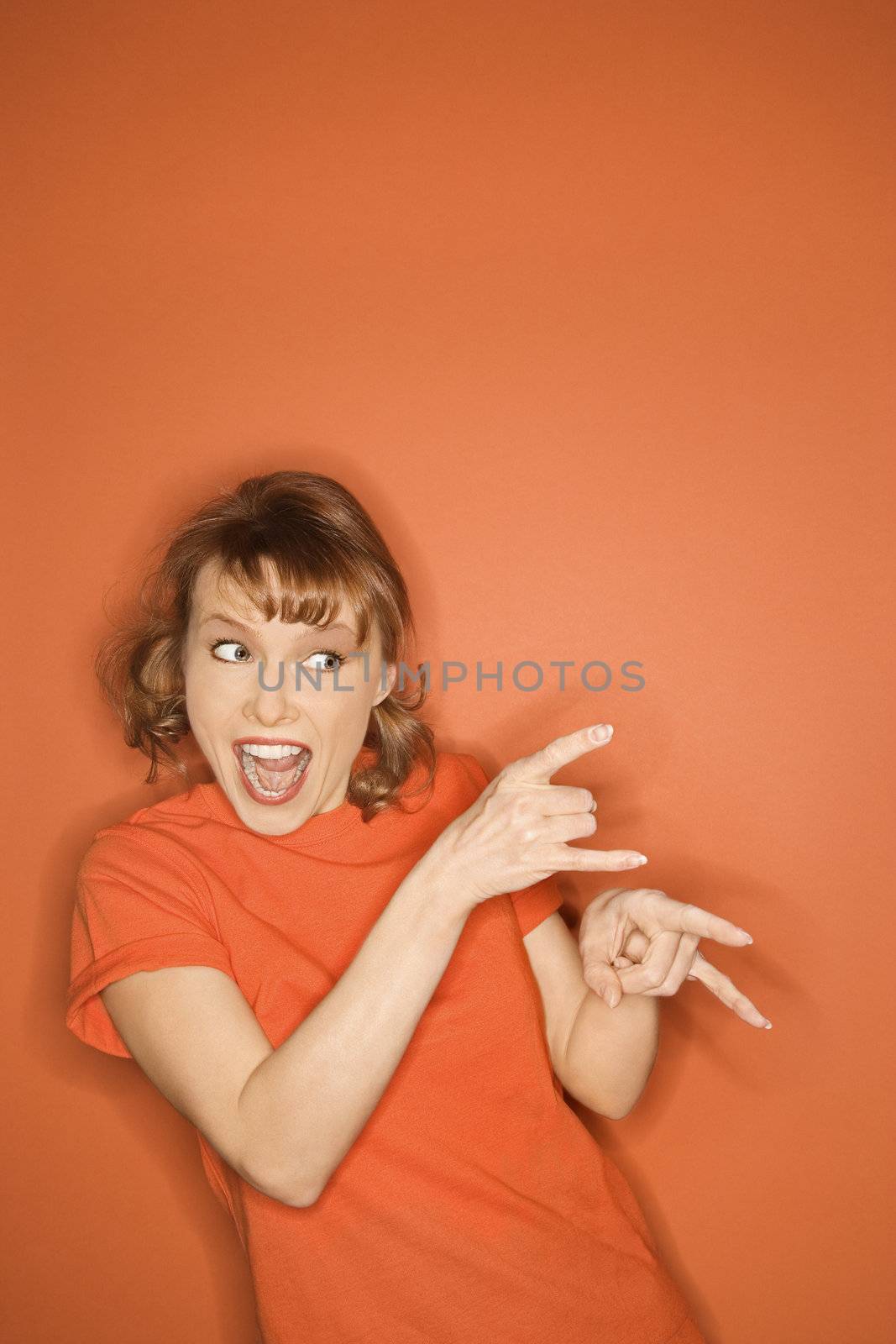 Smiling Caucasian mid-adult woman gesturing on orange background.