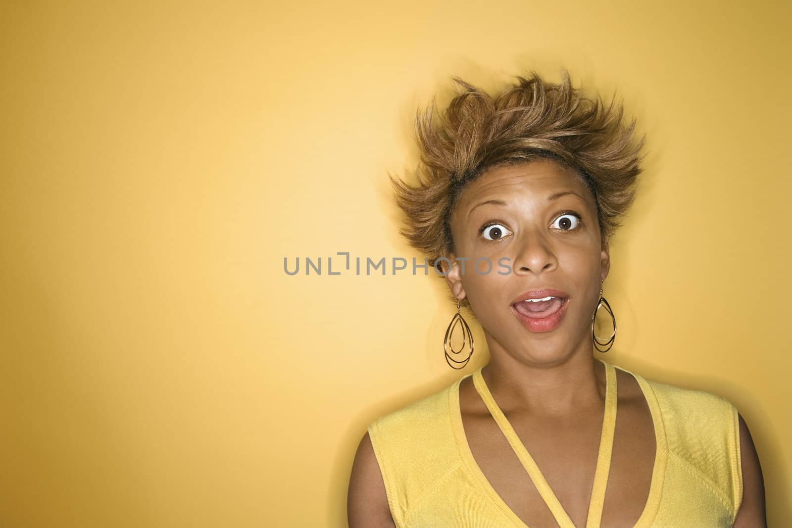 Portrait of surprised African-American young adult woman on yellow background.