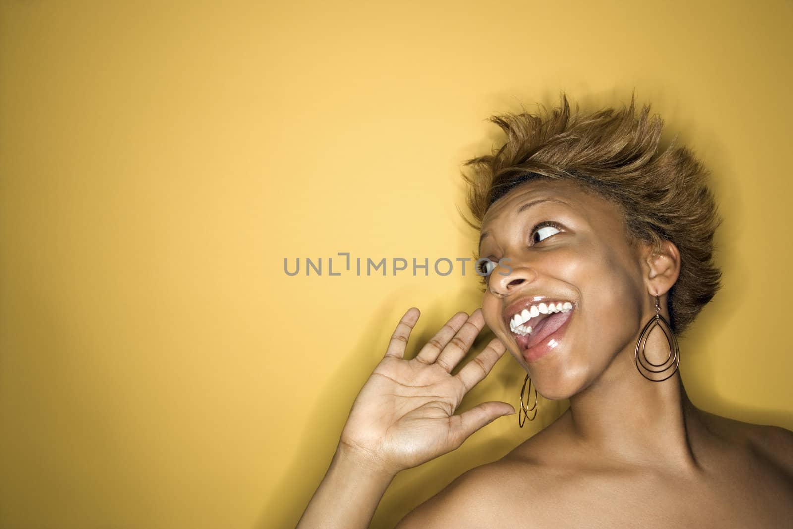 Portrait of young African-American woman on yellow background yelling and smiling at someone.