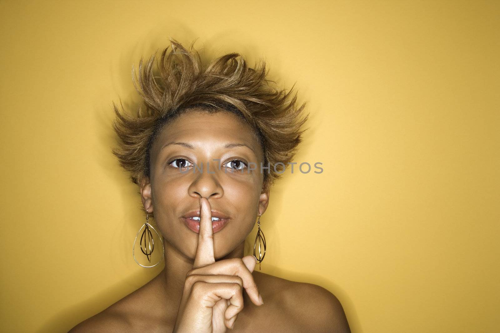 Portrait of young African-American adult woman on yellow background quieting the viewer.