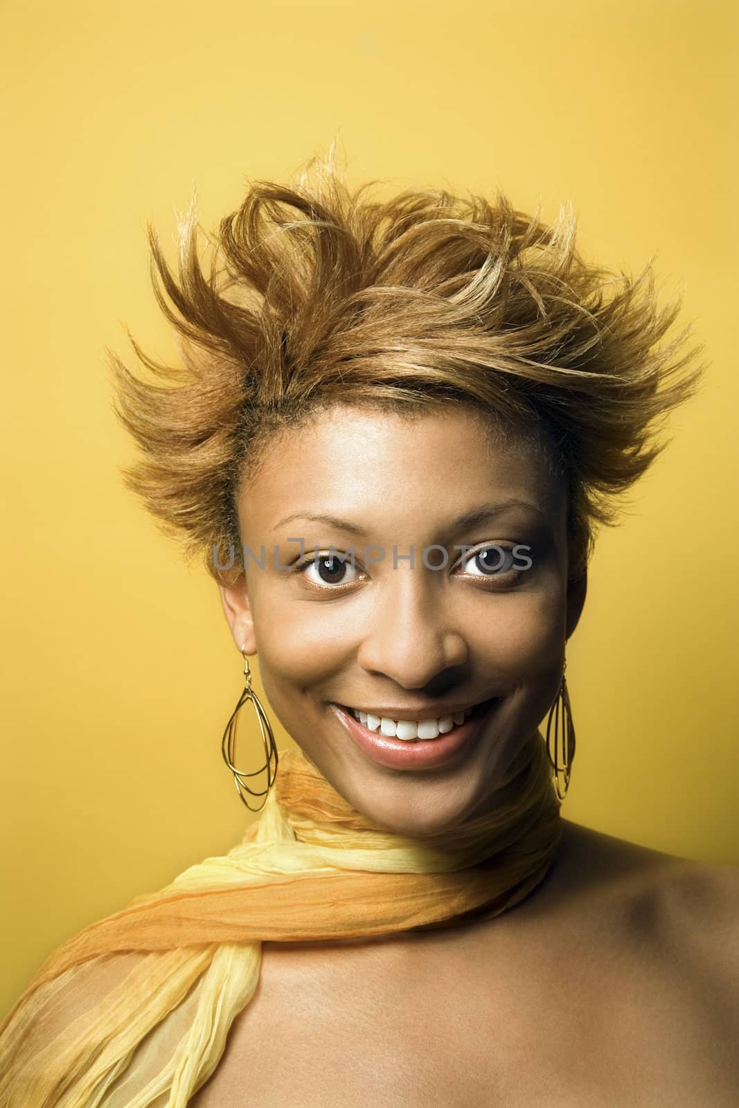 Head and shoulder portrait of smiling young African-American adult woman on yellow background.