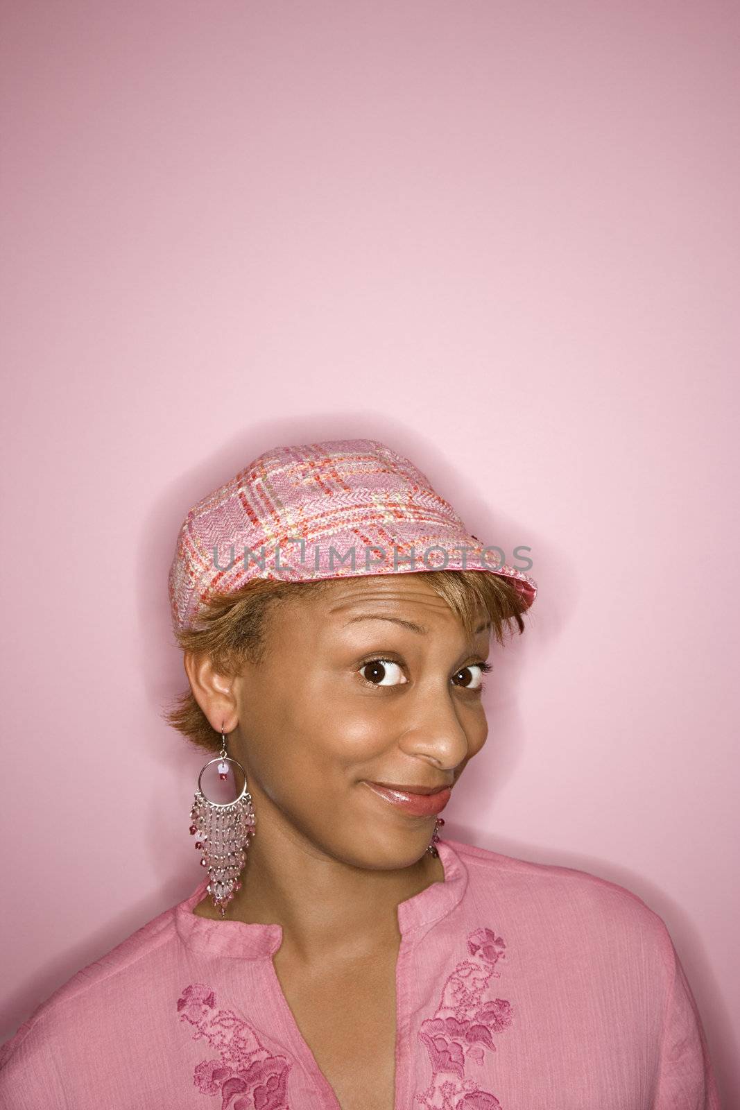Portrait of young African-American woman on pink background with comical expression on her face.