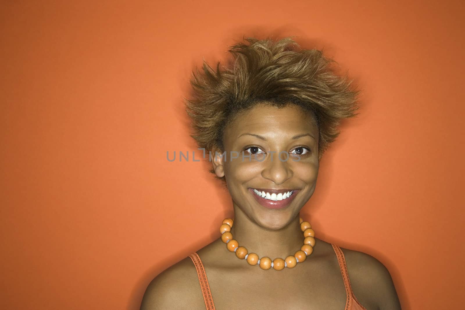 Portrait of smiling young African-American adult woman on orange background.