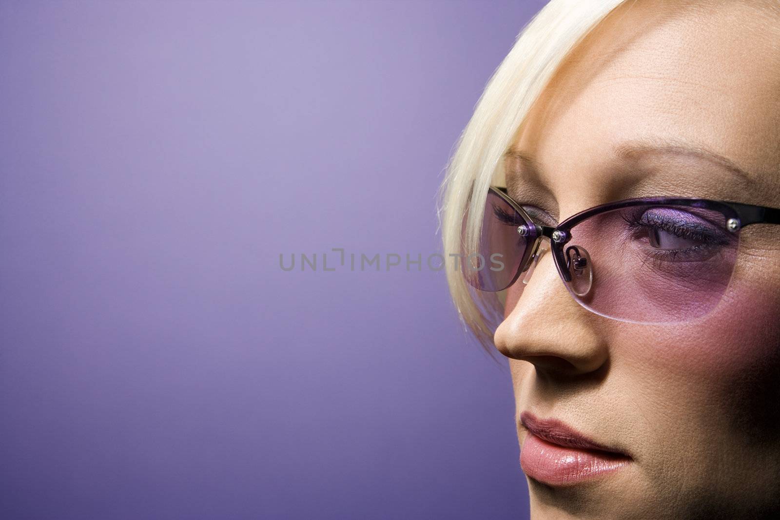 Close-up portrait of young adult Caucasian blond woman on purple background wearing sunglasses.