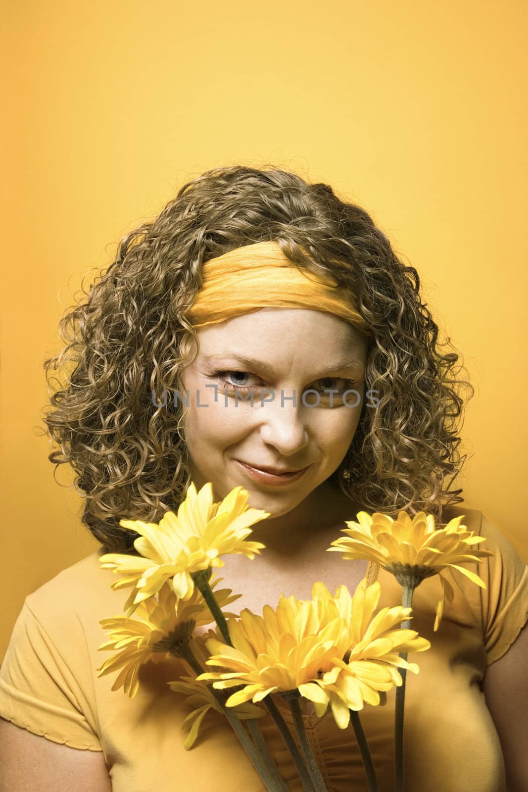 Portrait of young adult Caucasian woman on yellow background holding bouquet of flowers.