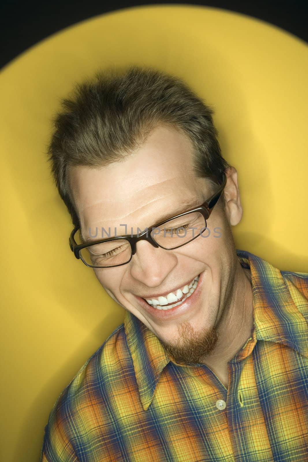 Vignette of adult Caucasian man on yellow background laughing.