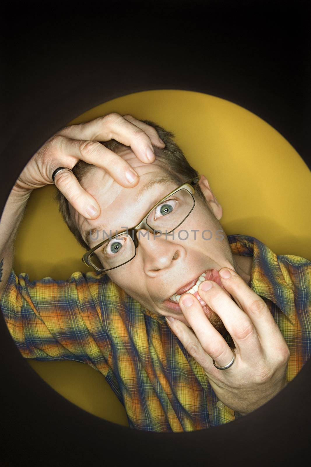 Vignette of adult Caucasian man on yellow background pulling at face and looking stressed out.