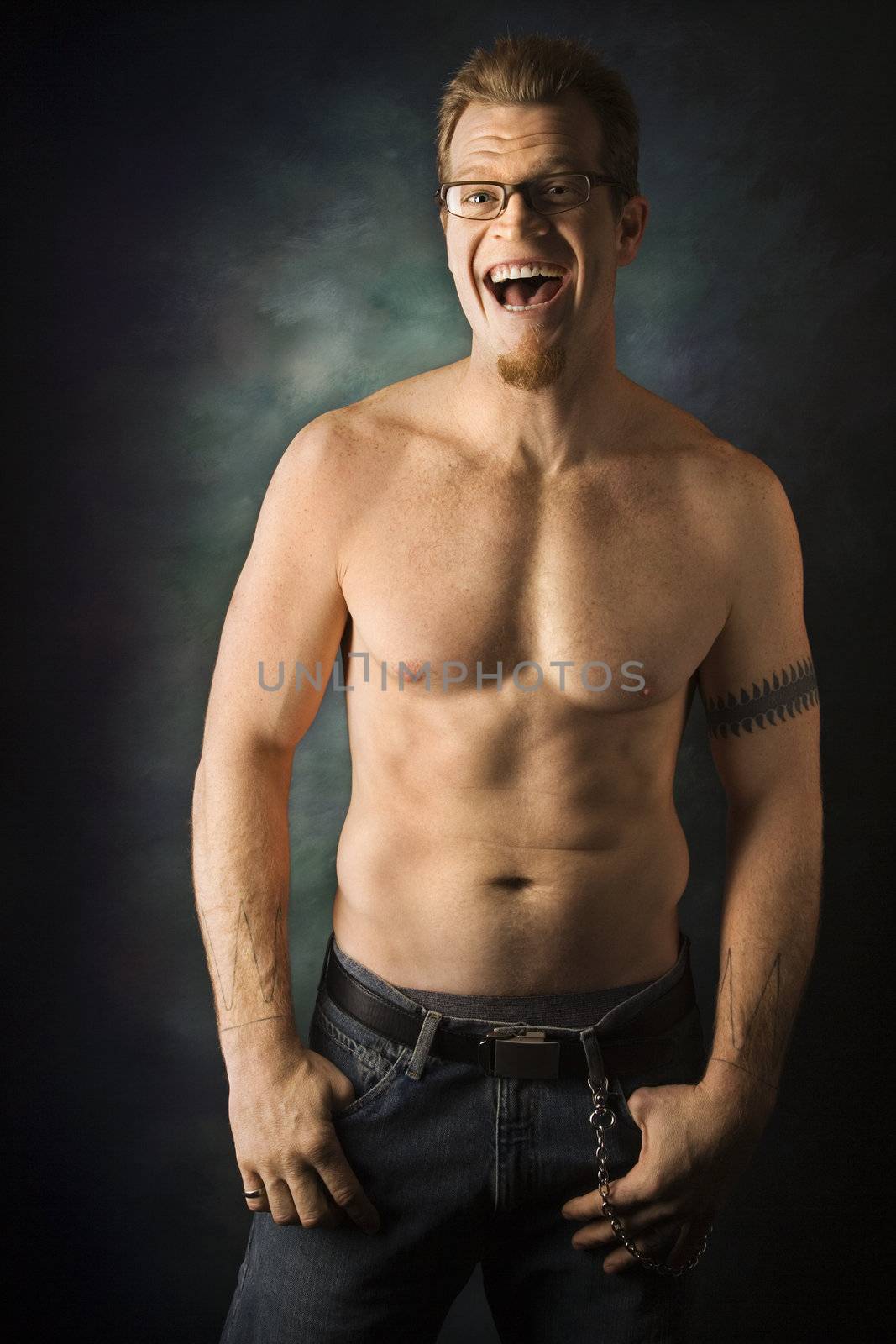 Portrait of shirtless adult Caucasian man on studio background laughing.