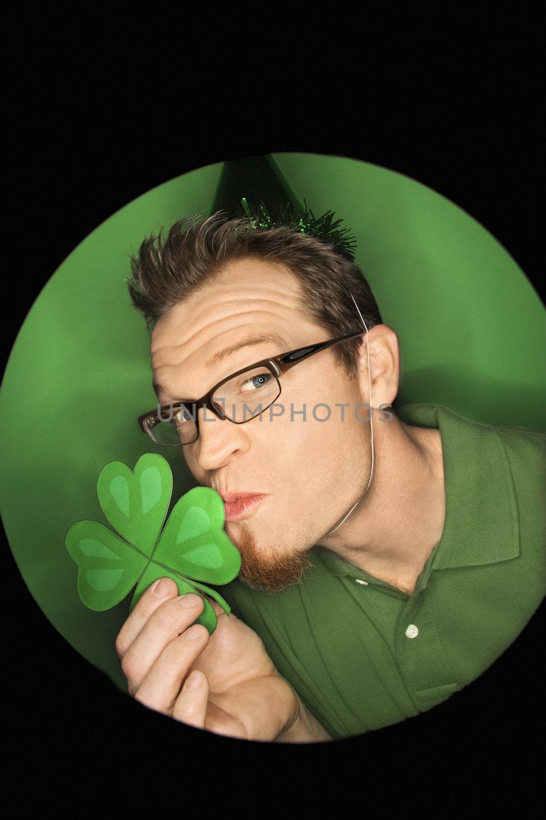 Vignette of adult Caucasian man on green background wearing Saint Patricks Day hat and kissing shamrock.