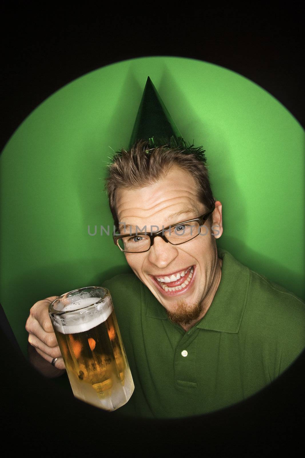 Vignette of adult Caucasian man on green background wearing green hat and holding beer.
