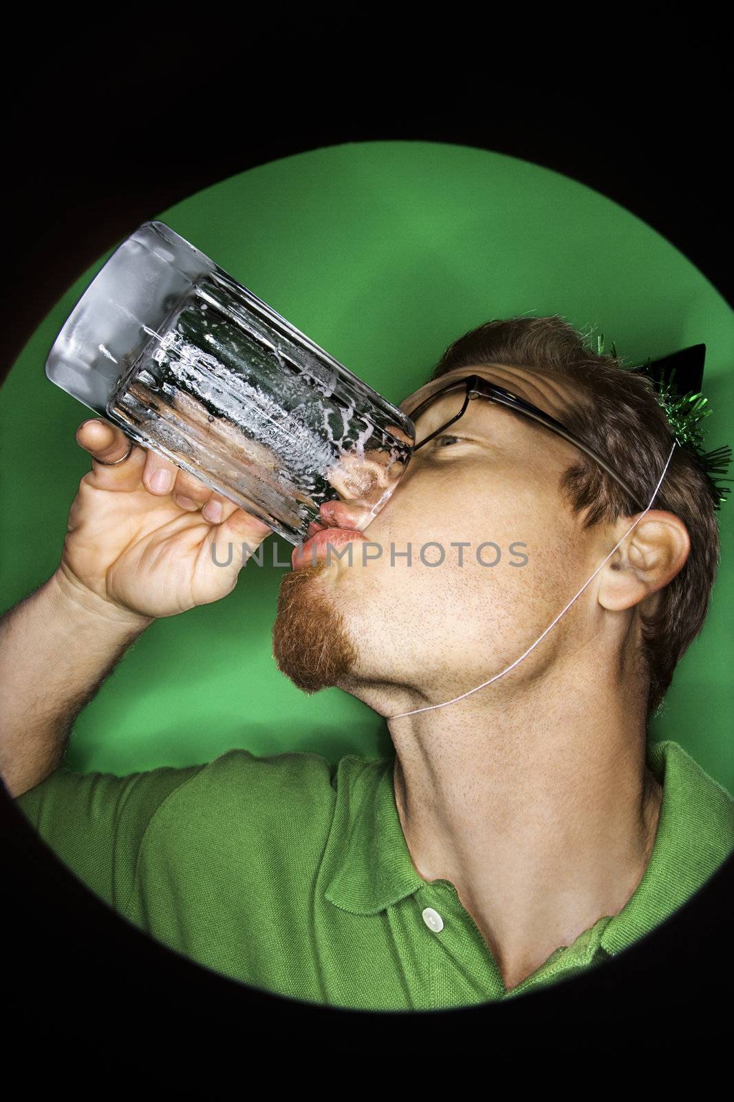 Vignette of adult Caucasian man on green background wearing green hat and drinking beer.
