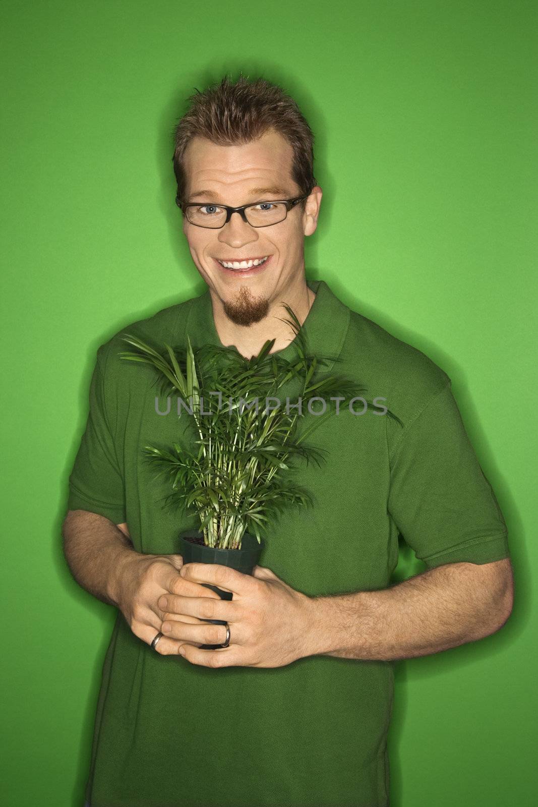 Portrait of smiling adult Caucasian man on green background holding plant.