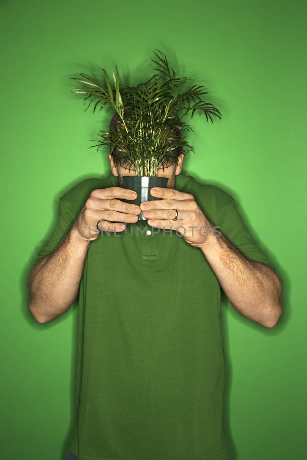 Portrait of adult Caucasian man on green background holding plant in front of his face.
