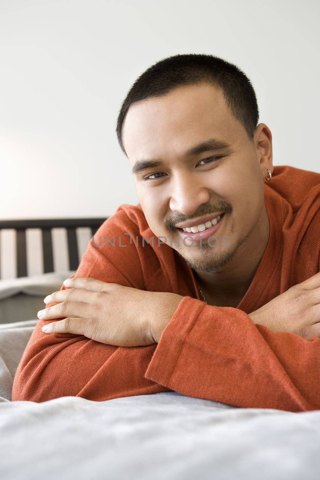 Close-up of Asian young adult man lying on bed looking at viewer smiling.